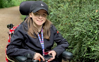 A girl dressed in all black sitting in a red mobility chair smiling.