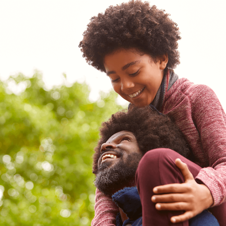 man with afro smiling up at child on his shoulders