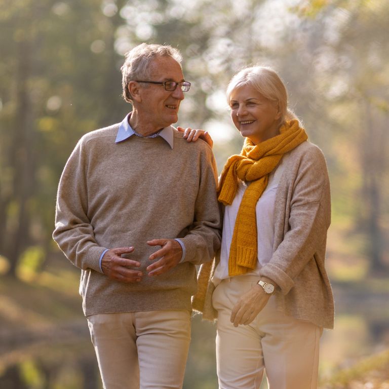 grey haired man and grey haired woman in beige outfits walking in nature