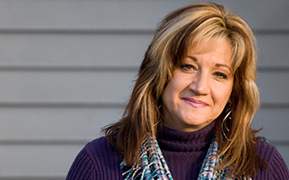 woman with brown and blonde hair in a purple sweater smiling