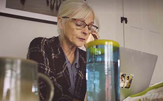 Woman with blonde hair and glasses sitting at a table on the phone and computer