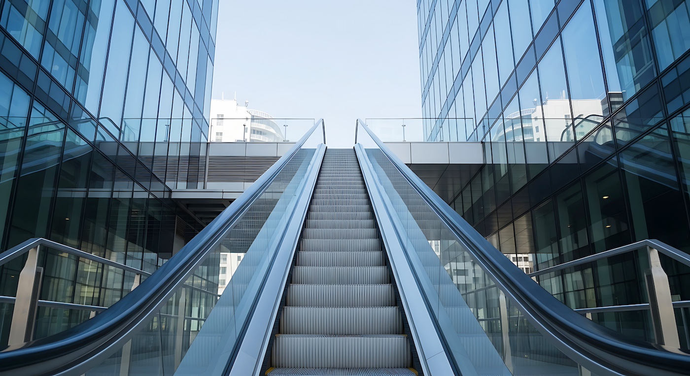 Escalator leading upwards between glass office buildings