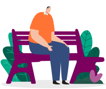 A man sitting on a bench, alone. His hands rest on his lap, and he looks down towards the ground.